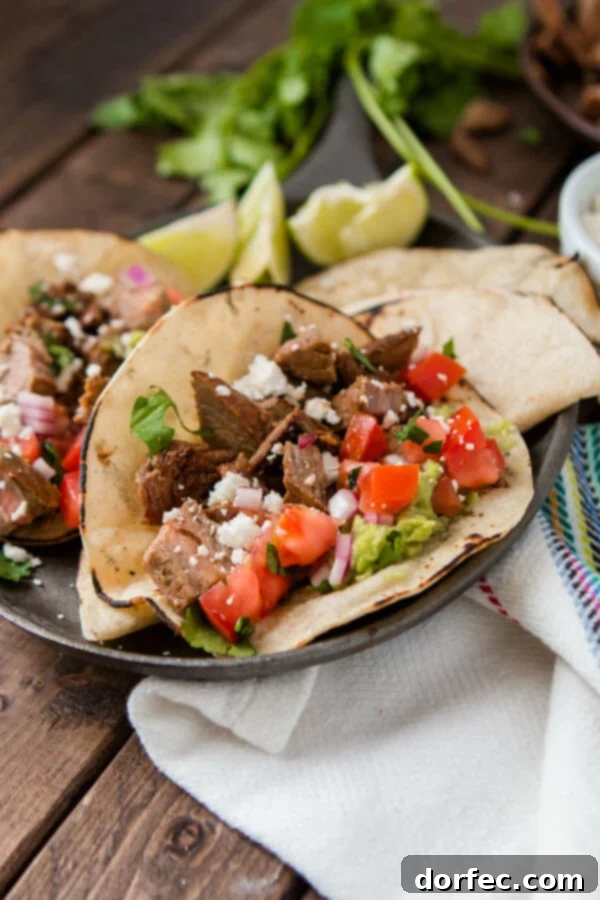 Two authentic carne asada tacos elegantly presented on a serving plate atop a rustic wooden table.