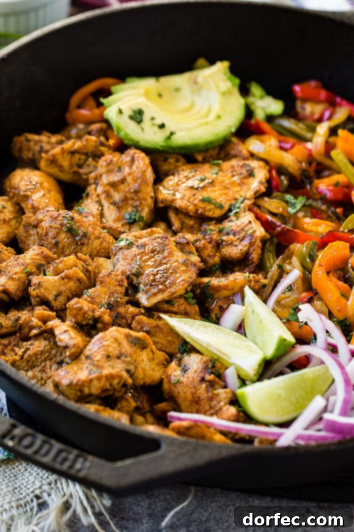 A tantalizing photo of a cast iron skillet filled with savory chicken fajita filling, featuring perfectly cooked chicken, sautéed peppers and onions, fresh lime wedges, sliced purple onion, and creamy avocado slices.