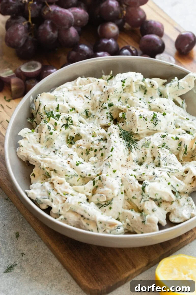 Close-up of shredded chicken salad in a serving bowl with tarragon and dill.