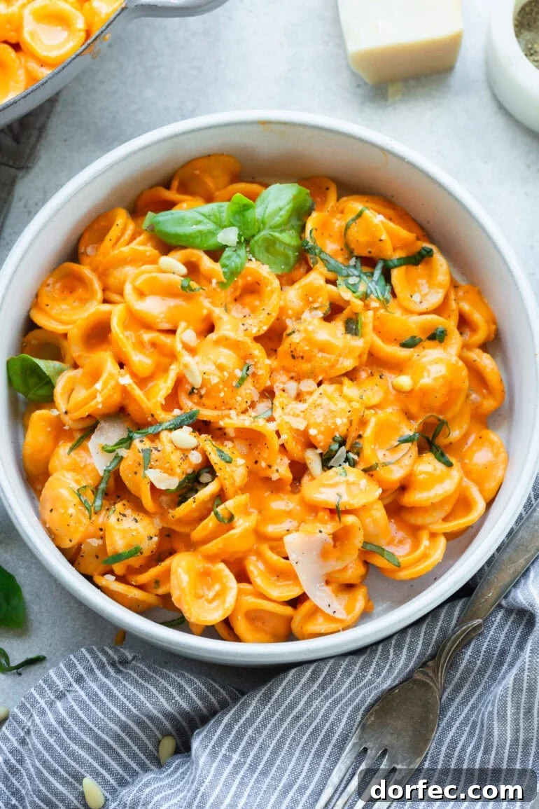 a large bowl of cooked orecchiette pasta tossed with roasted red pepper sauce and topped with chopped herbs 