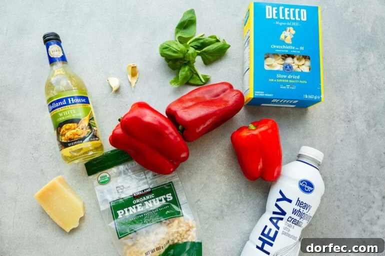 all the ingredients for roasted red pepper pasta sitting on table including red bell peppers, heavy cream, pasta, fresh basil, garlic gloves and parmesan cheese