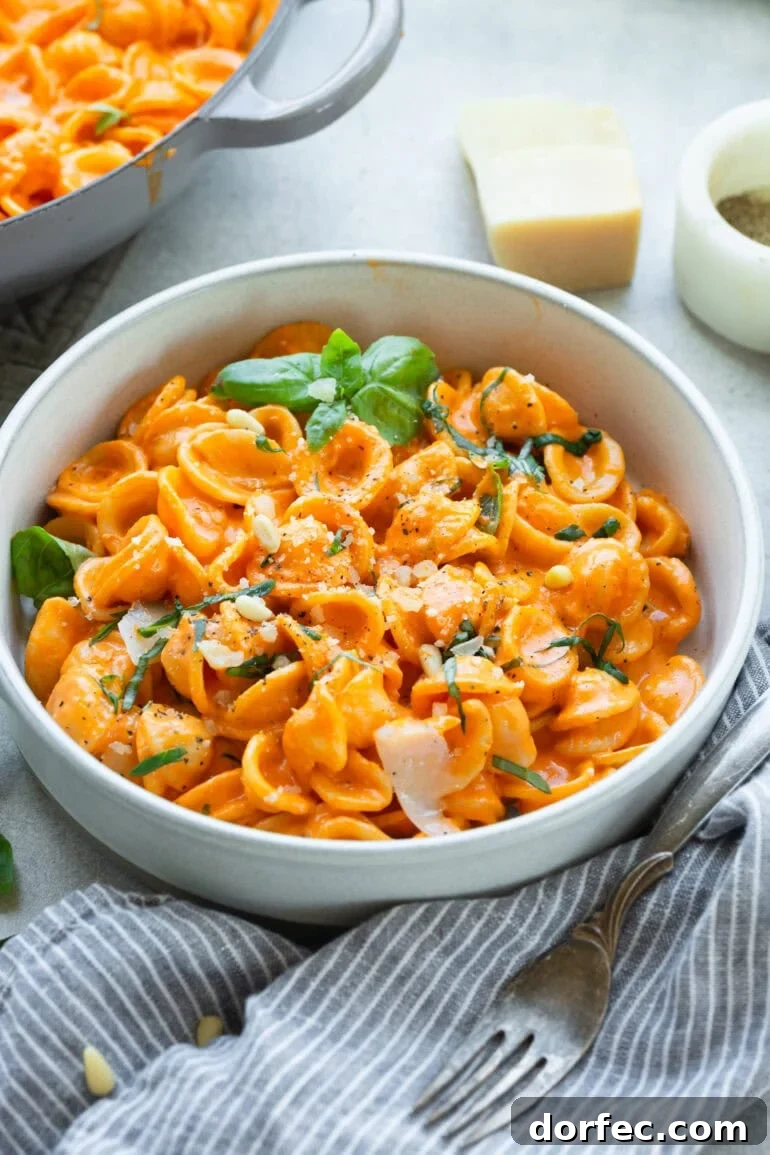 a bowl of creamy red pepper pasta topped with fresh basil and shaved parmesan cheese