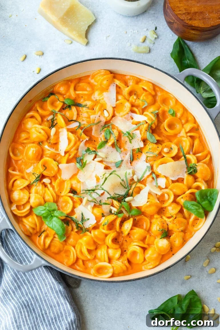 a large dutch oven full of cooker oreicchete pasta mixed in a creamy roasted red pepper sauce and topped with shaved parmesan, chopped basil and toasted pine nuts