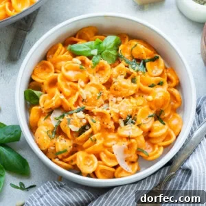 a large bowl of cooked orecchiette pasta tossed with roasted red pepper sauce and topped with chopped herbs