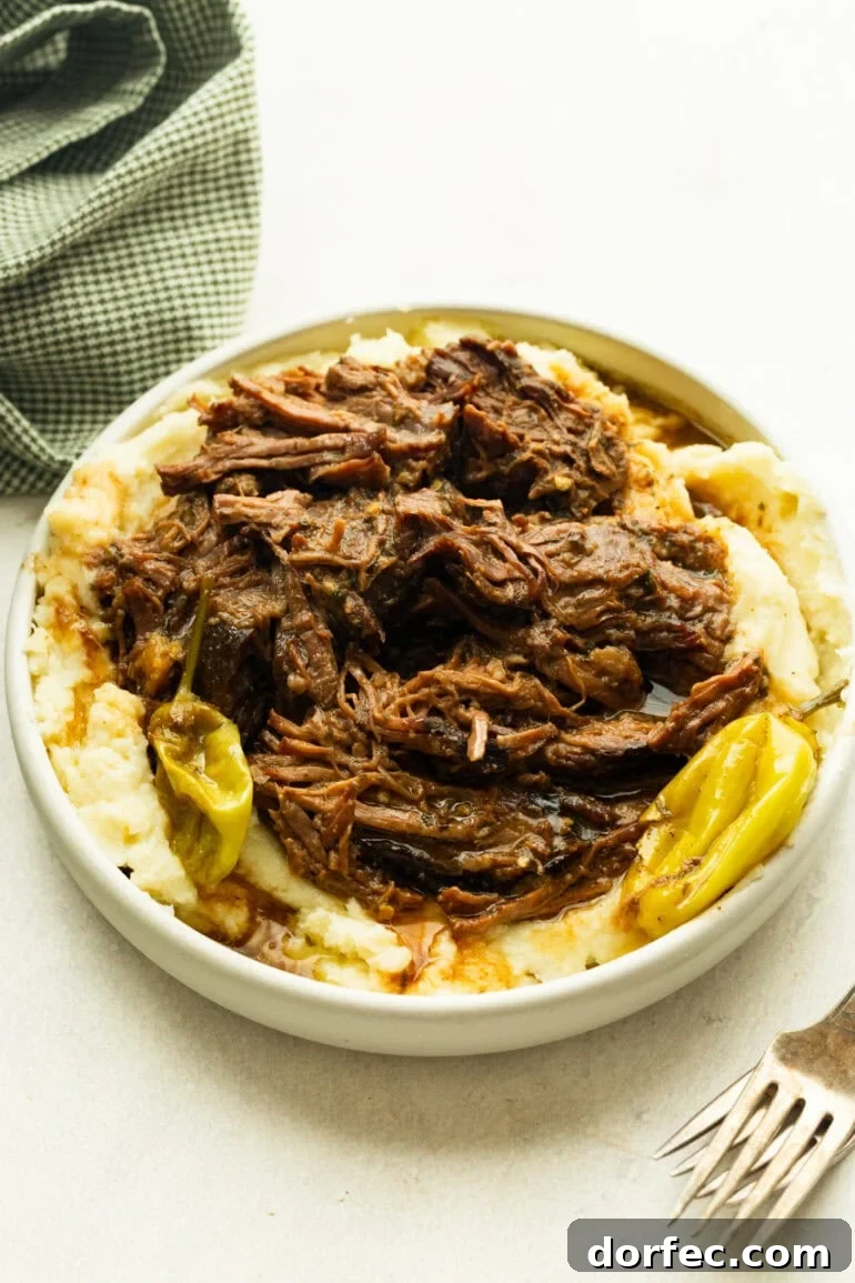 Mississippi Pot Roast Slow Cooker Recipe for Tender, Flavorful Beef 6 a large serving bowl full of juicy, tender beef served over the top of creamy mashed potatoes and whole pepperoncicnis around the bowl