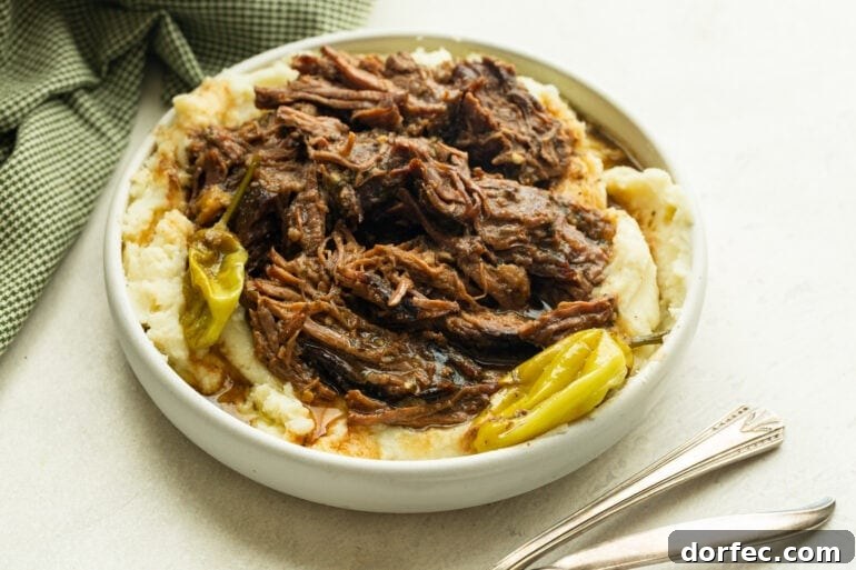 Mississippi Pot Roast Slow Cooker Recipe for Tender, Flavorful Beef 7 a large serving bowl of creamy mashed potatoes with juicy shredded pot roast on top and a few whole pepperoncinis