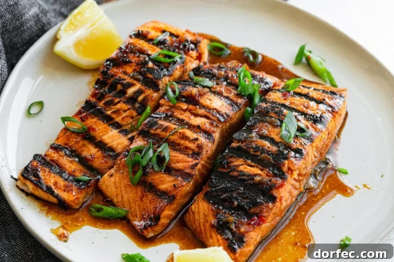 three grilled salmon filets sitting on a white plate sitting in a saucy marinade
