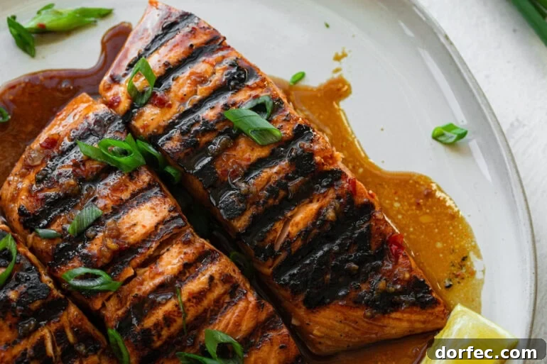 two grilled salmon filets sitting in a marinade sauce on a white plate and topped with chopped green onions