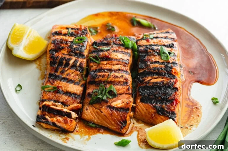 three marinated grilled salmon filets sitting on a white plate with a slice of lemon next to it and chopped green onions