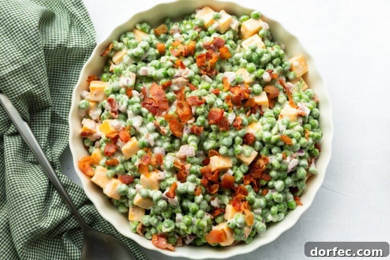 a large serving bowl full of creamy pea salad with bacon bits, red onions, and cheddar cheese