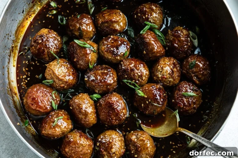 a large skillet full of browned meatballs in a sticky sauce and topped with chopped green onions and sesame seeds