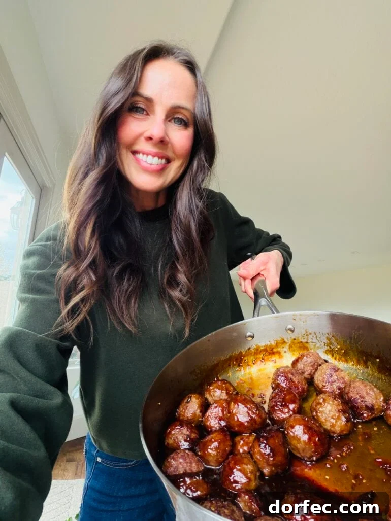 Carrian holding a large skillet with browned meatballs coated in a sticky sauce