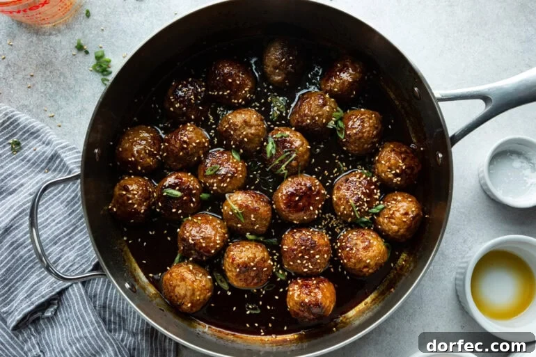 a large skillet full of saucy korean meatballs topped with sesame seeds and chopped green onions