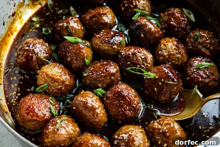 several golden brown meatballs sitting a thick stick sauce and topped with sesame seeds and green onions
