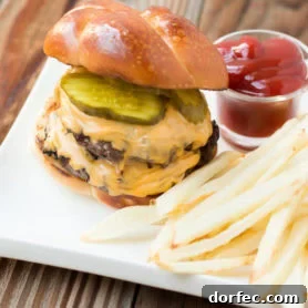 a cheeseburger with two patties, and pickles sitting next to french fries and a small cup of ketchup