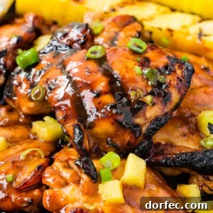 A photo of grilled huli huli chicken with grilled pineapple in the background.