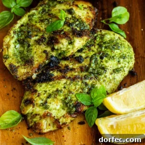 two grilled chicken breasts coated in basil sitting on a cutting board with lemon wedges