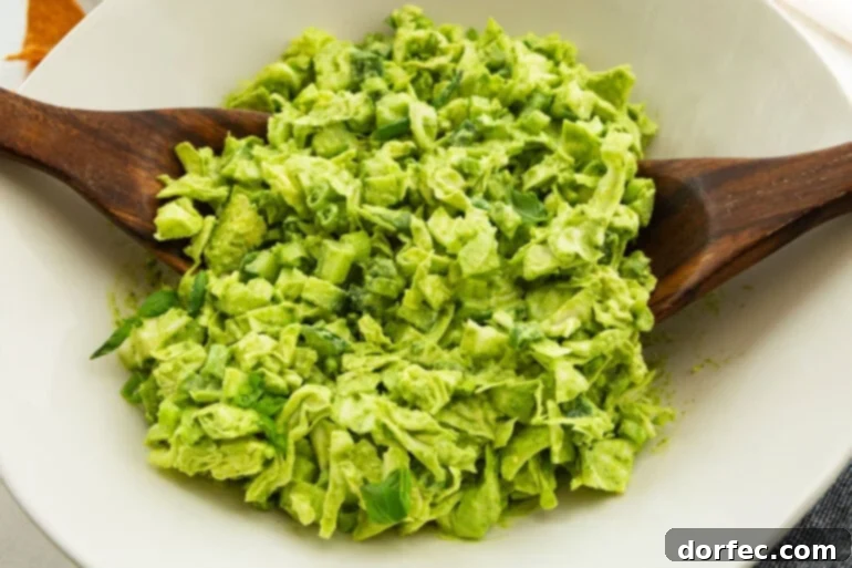 A large white bowl of chopped green goddess salad being tossed with wooden spoons.
