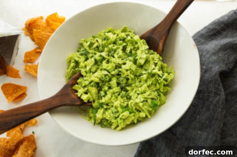 Tossing the chopped green goddess salad in a white serving bowl, showing the creamy dressing coating the vegetables.