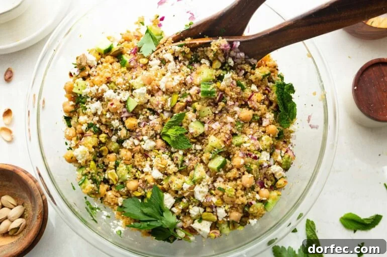 a large glass bowl full of a chickpea, quinoa and cucumber salad with red onions and feta cheese