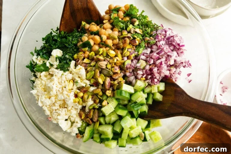 all the ingredients for a viral jennifer aniston salad being stirred together with wooden salad tongs