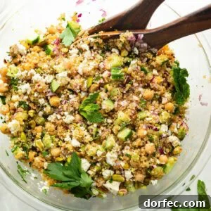 a large glass bowl full of a chickpea, quinoa and cucumber salad with red onions and feta cheese