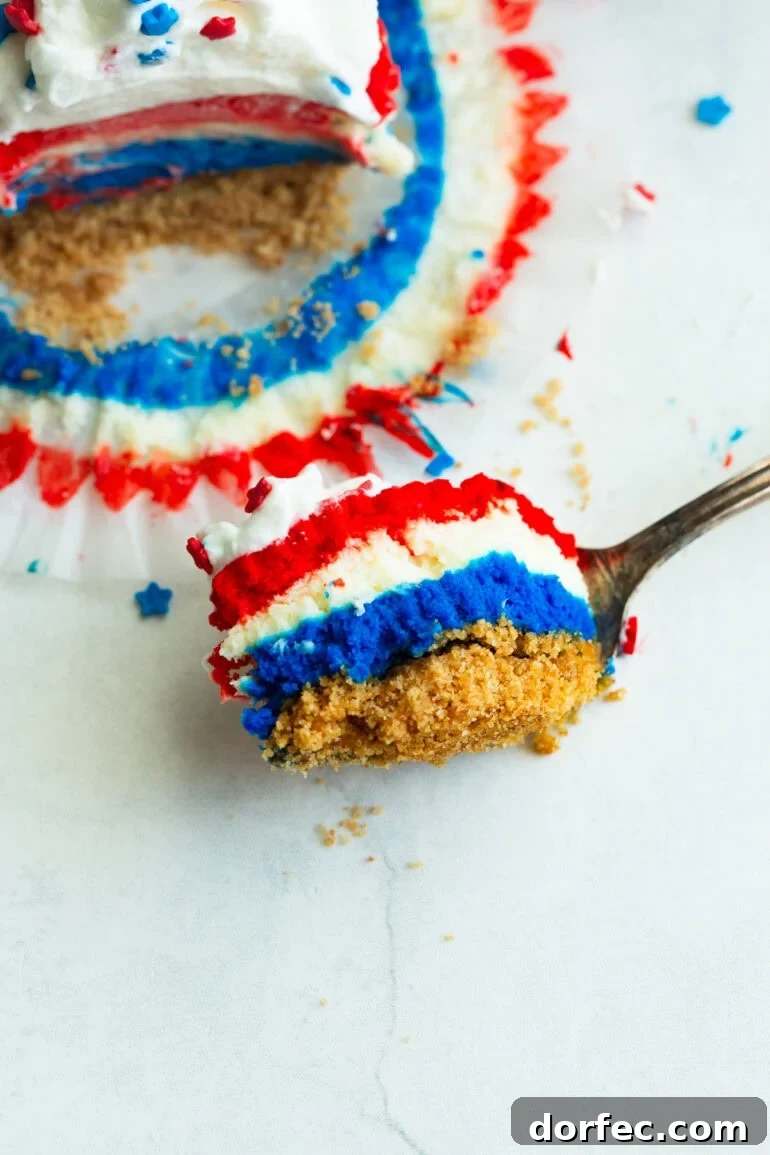a fork with a bite of layered red, white, and blue cheesecakes with a swirl of whipped cream and patriotic star sprinkles