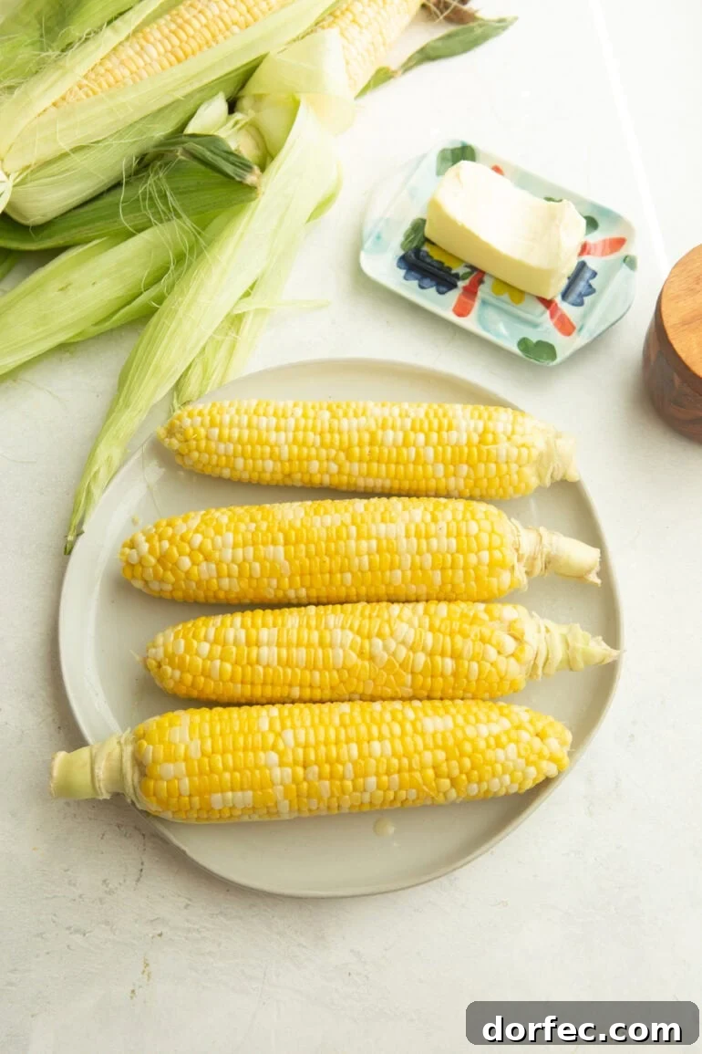 four ears of corn on a plate with a stick of butter next to the plate