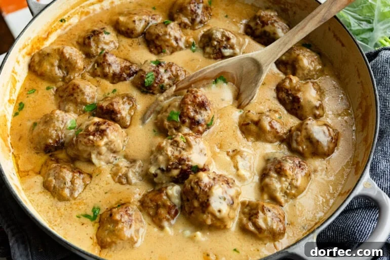 Authentic Swedish Meatballs with Creamy Gravy 6 swedish meatballs sitting in thick gravy sauce being stirred with a wooden spoon
