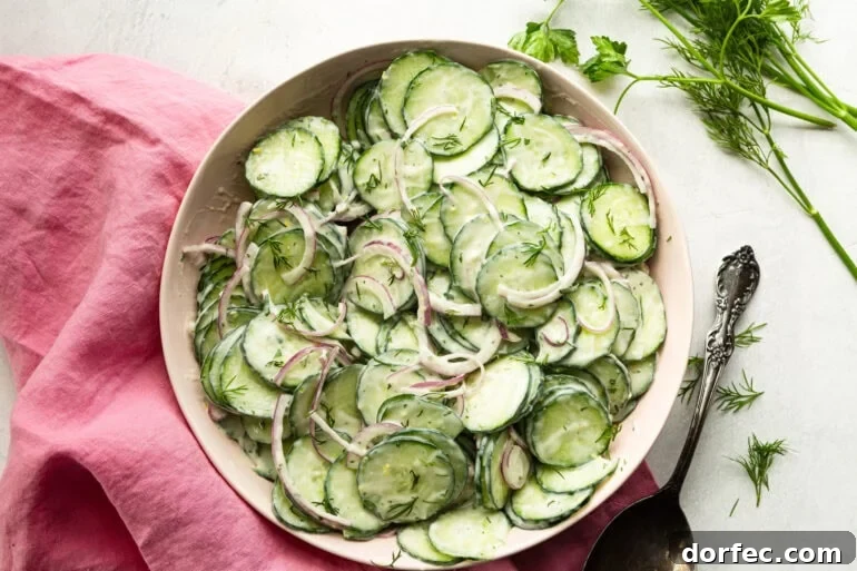 A close up of creamy cucumber salad showing thin cucumber slices and red onion tossed in a thick creamy dill dressing garnished with fresh basil.