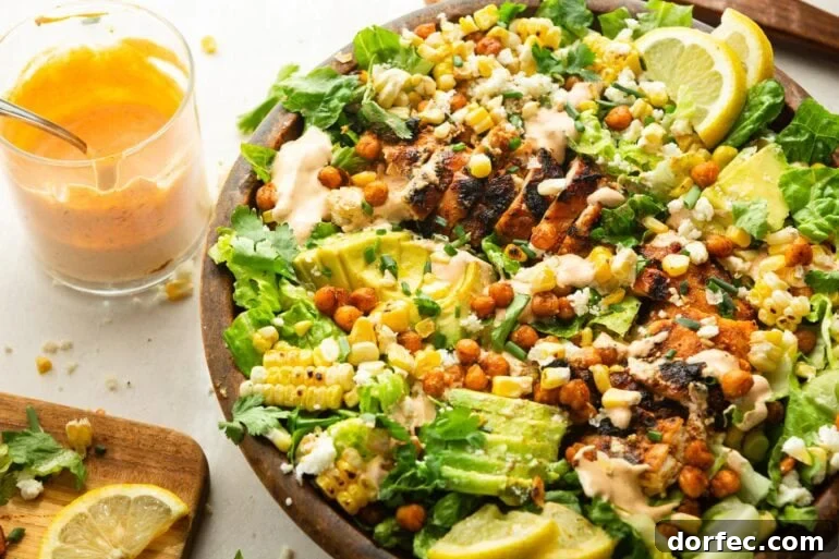 a large wooden bowl  grilled chicken salad topped with sliced avocado, crispy chickpeas and drizzled with southwest ranch