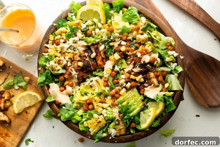 a large wooden bowl full of grilled chicken breast, sliced avocado, corn, crispy chicken peas and drizzled with southwest ranch