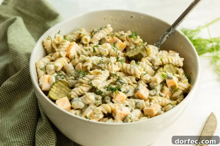 A large bowl of dill pickle pasta salad with noodles in a creamy sauce, pickles, and cheddar cheese