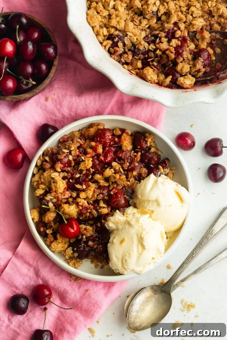 Homemade Old Fashioned Cherry Crisp Recipe 4 a serving of cherry crisp on a small dessert plate with two scoops of vanilla on the side and the whole cherry crisp in a baking dish sitting next to the plate