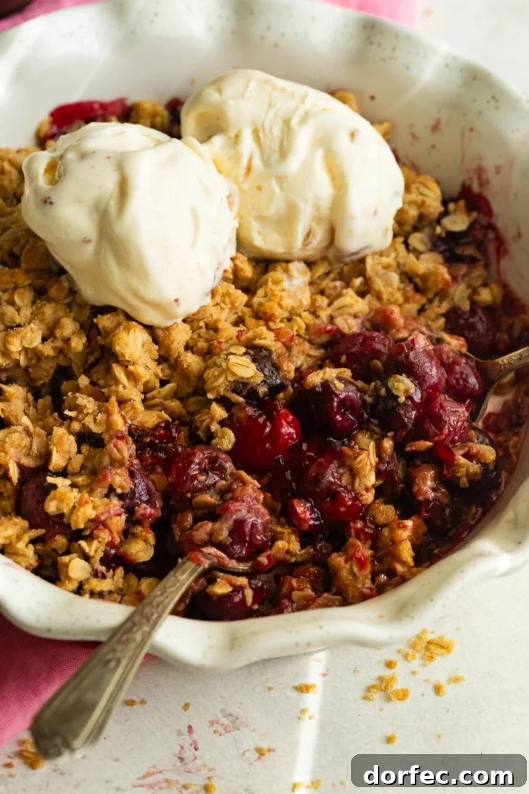 Homemade Old Fashioned Cherry Crisp Recipe 6 someone scooping up a bite of cherry crisp topped with scoops of vanilla ice cream